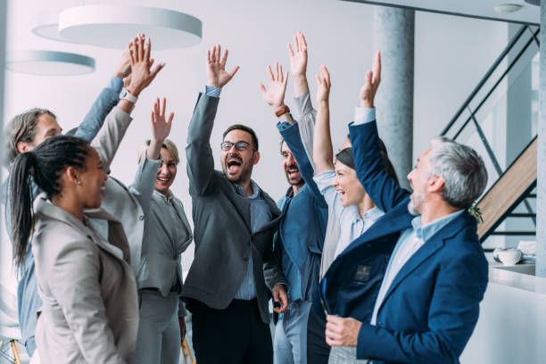 Shot of group of business people celebrating their success in the office. Multiracial group of corporate business persons on a business meeting in board room. Cheerful business team raising their hands together in the air.